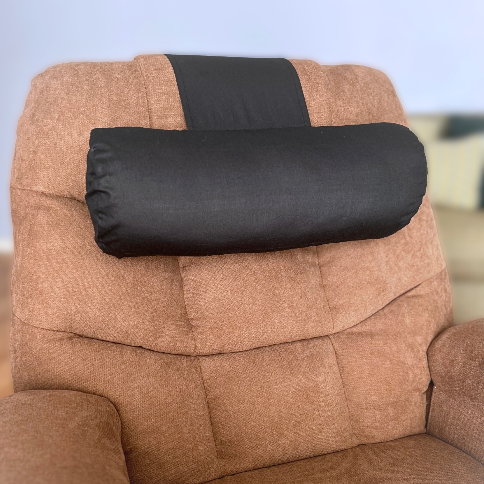 EOT Wellness black recliner pillow with weighted tail, positioned in the headrest position on a brown upholstered chair.